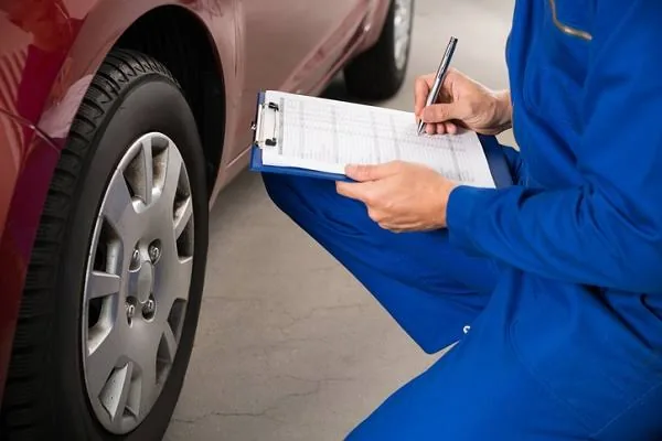 An inspector filling out a checklist beside a vehicle's front wheel
